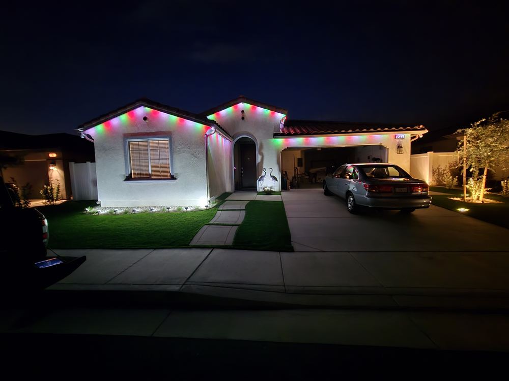 Home decorated with red, green and white Christmas lights along the roofline and yard